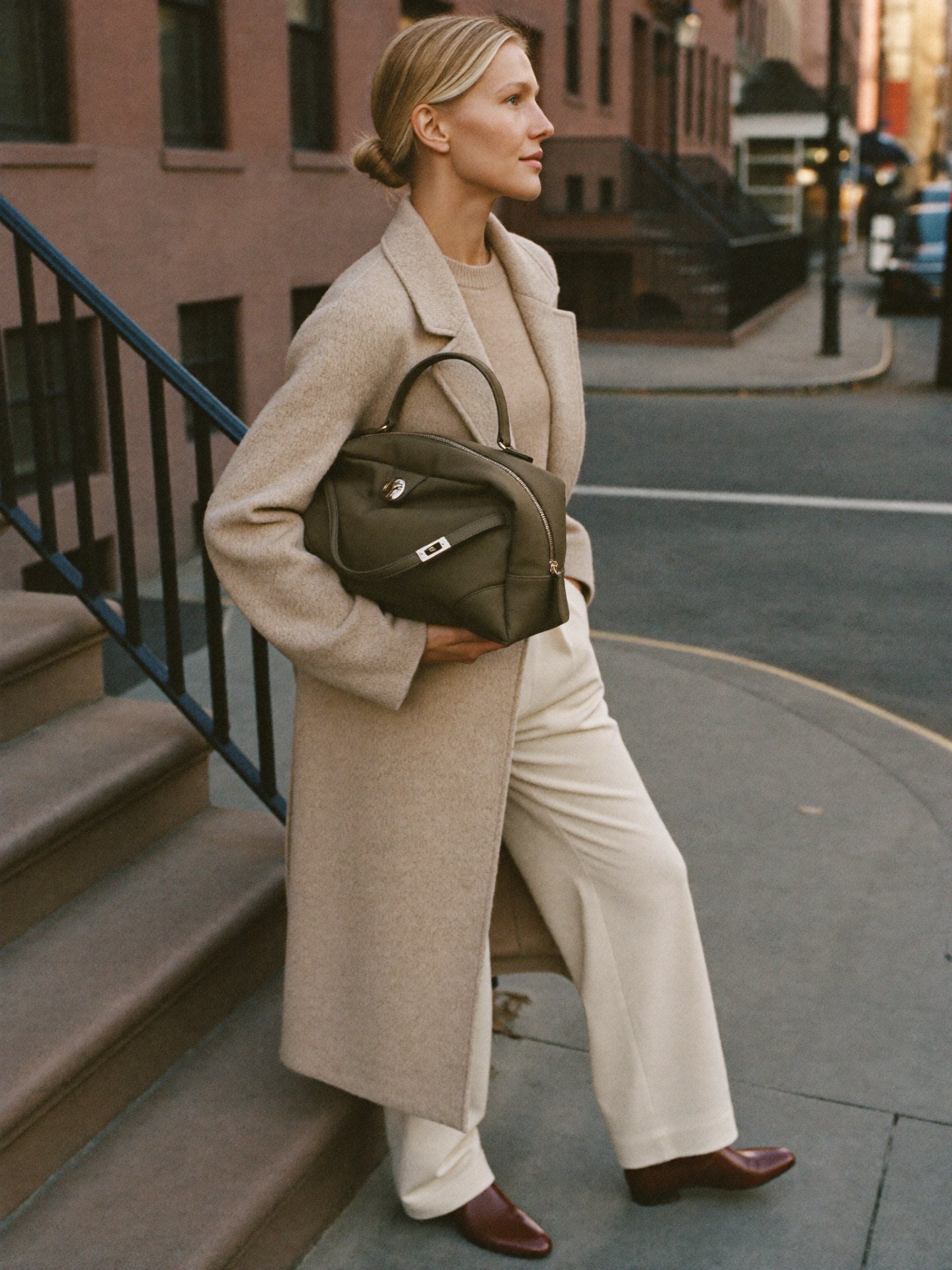 Woman standing NYC brownstone golden hour with The Slouch in Olive premium nylon by Bowryn — warm beige editorial